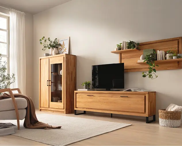 Wohnzimmer mit Wohnwand aus Massivholz, Lowboard, Vitrine und Wandregal in Eiche Natur, kombiniert mit Fernseher und dekorativen Pflanzen für eine moderne und wohnliche Einrichtung.